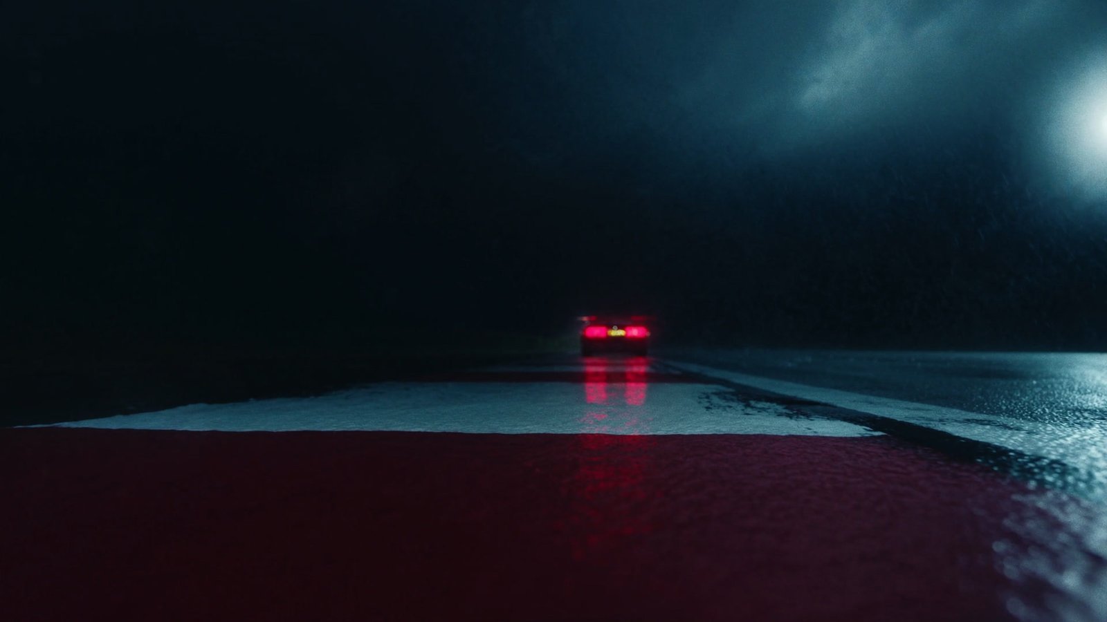 Brake lights reflected across a wet kerb at the apex of a night corner
